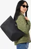 A woman is wearing a green jacket and carrying a black tote bag over her shoulder. Produktbild-Vorschau