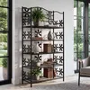 A black metal shelf unit with decorative flower cutouts, filled with books and decorative vases, placed indoors next to a large window. Náhled obrázku produktu