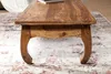 A close-up of a wooden coffee table with ornate legs, resting on a patterned rug. Podgląd zdjęcia produktu