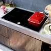A modern kitchen countertop with a built-in induction hob, featuring a red pot and some garnishes. Podgląd zdjęcia produktu