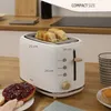 A white toaster with bread inside, placed on a wooden countertop with some food items and a mug. Produktbild-Vorschau