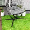 A hanging egg chair with cushions sits on a green lawn next to potted plants. Produktbild-Vorschau