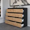 A modern dresser with eight drawers, featuring a black matte frame and oak-effect drawer fronts, displayed in a room setting with a mirror and artwork. Produktbild-Vorschau