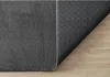 The underside and edge of a dark gray rug are shown, with the rug partially covering a light brown wooden floor. Produktbild-Vorschau