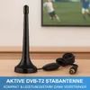 A black DVB-T2 antenna with its cable and connector is placed on a wooden surface, with a blurred television screen showing a soccer game in the background. A blue banner with text is at the bottom. Produktbild-Vorschau