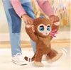 A child's hands are holding a toy monkey, which is standing and appears to be walking. Produktbild-Vorschau