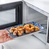 A hand is placing a plate of sushi into an open microwave. Náhled obrázku produktu
