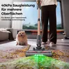 A person is using a cordless vacuum cleaner to clean up a mess on the floor, with a dog watching. Produktbild-Vorschau
