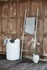 A white laundry basket and a white towel ladder stand against a rustic wooden door, with a vase of pink magnolia flowers nearby. Produktbild-Vorschau