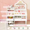 A white vanity table with various toy makeup and accessories, set against a pink striped background. Voir les images du produit