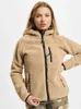 A woman wearing a beige teddy fleece jacket with black zippers and trim, standing against a light gray background. Produktbild-Vorschau