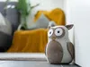 A decorative owl doorstop is placed on the floor next to a white wall, with a blurred living room in the background. Anteprima dell’immagine prodotto
