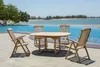 A wooden table and chairs set is placed on a patio next to an infinity pool with a view of the ocean and trees. Produktbild-Vorschau