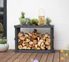 A dark gray firewood rack filled with logs, placed on a wooden deck against a white wall. Several potted plants and a lantern are on top of the rack. Podgląd zdjęcia produktu