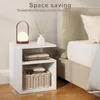A white bedside table with a lamp, vase, and books next to a bed. Produktbild-Vorschau