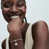 A woman is smiling and showing off a bracelet with a charm. Produktbild-Vorschau