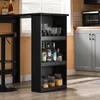 A black shelving unit with bottles and glasses on shelves, next to a bar counter and stool. Produktbild-Vorschau