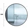A round mirror reflecting a modern bathroom with a view of the ocean and a chair. Produktbild-Vorschau