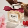 A bottle of Chloe Signature Intense perfume is displayed on a textured surface, with a pink flower and raspberries in the foreground and a piece of driftwood in the background. Anteprima dell’immagine prodotto