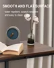 A close-up of a dark wood-grain table surface with a book, a decorative clock, and a vase with cotton stems. Produktbild-Vorschau