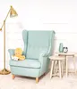 A teal wingback chair with a yellow octopus plush toy on it, next to two small beige side tables with a vase and an alarm clock on them. A gold floor lamp is to the left. Anteprima dell’immagine prodotto
