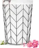 A laundry basket with a white liner and a black geometric metal frame, placed on a white background with some decorative flowers and cotton bolls. Produktbild-Vorschau