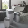 Three trash cans of different sizes are placed on a carpeted floor next to a radiator and a window. A desk with office supplies and a chair are visible in the background. Anteprima dell’immagine prodotto