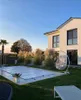 A backyard scene with a covered swimming pool, a modern house, and outdoor furniture. Produktbild-Vorschau