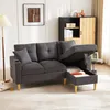A dark gray sectional sofa with its storage compartment open, revealing stored items. The sofa is in a living room setting with a floor lamp and a cabinet in the background. Podgląd zdjęcia produktu