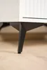 Close-up of the black metal legs of a white cabinet or furniture piece, resting on a light wooden floor. Produktbild-Vorschau
