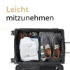 An open suitcase packed with clothing and shoes, with a white charging station placed on top of a folded shirt. Produktbild-Vorschau