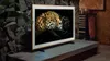 A Samsung Frame TV displaying a jaguar and a black panther, placed on a stand in a rustic living room setting. Produktbild-Vorschau