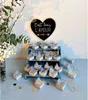 A display of small gift boxes decorated with butterflies, arranged on a tiered shelf and on a table, with a floral arrangement and a heart-shaped sign in the background. Produktbild-Vorschau