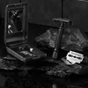 A black Störtebekker razor and blades are displayed on dark, textured rocks, with an open black case containing a mirror and accessories. Voir les images du produit