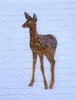 A decorative metal fawn figurine with white spots, standing against a white brick wall. Produktbild-Vorschau