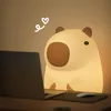 A capybara-shaped night light is placed on a desk next to a laptop, with a mouse and mousepad visible. Podgląd zdjęcia produktu