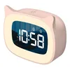 A pink digital alarm clock with a cat-ear design, displaying the time 10:58 PM, is shown against a white background. A person is visible sleeping in the background reflection on the clock's screen. Produktbild-Vorschau