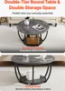 A round, double-tiered coffee table with a gray wood-like finish and black metal legs, shown in a living room setting with decorative items and storage. Voir les images du produit