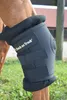A close-up of a horse's leg wearing a black support wrap, with a blurred background of grass and a fence. Produktbild-Vorschau