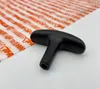 A black T-handle starter grip is placed on a white surface next to a sheet of clear plastic with orange text. Produktbild-Vorschau
