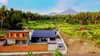 Two modern houses are situated in a lush, tropical landscape with palm trees and a volcano in the background. Podgląd zdjęcia produktu