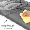 A close-up of a gray sleeping bag with water droplets on it, and a hand wiping it with a yellow cloth. Náhled obrázku produktu