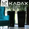 A living room scene with a teal armchair and two black planters with plants, set against a window view. Anteprima dell’immagine prodotto
