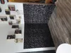 A room with a wall covered in black 3D decorative panels and a shelf with books. Produktbild-Vorschau