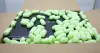A laptop is inside an open cardboard box, surrounded by green packing peanuts. Produktbild-Vorschau