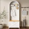 A white arched hall tree with a wooden bench and drawer, a white top hanging on a hook, a straw hat, a basket, and a paper bag on the top shelf. A plant is to the left, and an umbrella stand with umbrellas is to the right. Voir les images du produit