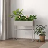 A planter with plants and flowers on a stand, next to a potted plant, in a room with curtains and wooden flooring. Voir les images du produit