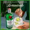 A bottle of Tanqueray London Dry Gin next to a cocktail with lime slices, with hands adorned with rings holding a cocktail stirrer. Produktbild-Vorschau