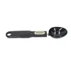 A black digital measuring spoon scale with a gold digital display and buttons, shown against a white background. Náhľad obrázku produktu