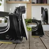 A collage of two images showing a black steam iron with a yellow soleplate, placed on a wooden surface. The background shows a kitchen setting with shelves and plants. Náhled obrázku produktu